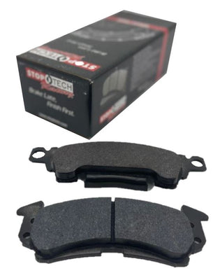 Black brake pad box in the background with 2 separate brake pads in the foreground on a white background